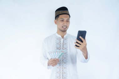 Moslem Asian man smiling happy while holding mobile phone and money clipart