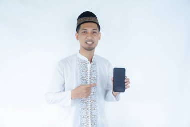 Müslüman Asyalı adam gülümsüyor ve elindeki boş cep telefonu ekranına işaret ediyor.