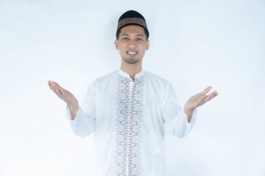 Müslüman Asyalı adam kolları açık kameraya gülümsüyor ve hoş geldin jesti yapıyor.