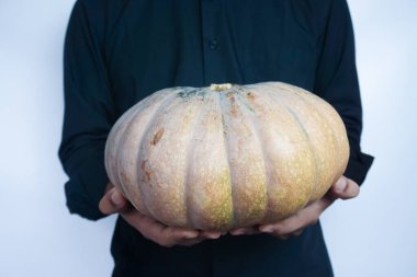 Elinde olgun, turuncu bir balkabağı tutan adam. Önden, yakın plan, beyaz arka plan izole edilmiş.