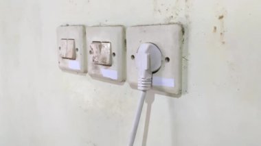 Genç yetişkin adam el ele tutuşuyor ve evdeki prizin prizine beyaz elektrik prizi takıyor. - Yakın çekim. Yan görünüm.