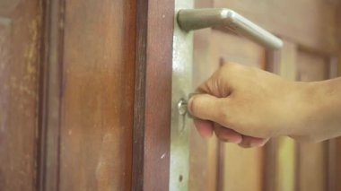 Ahşap kapıyı açan Asyalı eli. Asyalı bir adam kahverengi ahşap kapıyı açmaya çalışıyor. Paslanmaz çelik kapı kolu olan kapı..