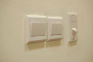a light switch, a plastic mechanical button of white color installed on a light wall with copy space for text.