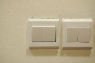 a light switch, a plastic mechanical button of white color installed on a light wall with copy space for text.