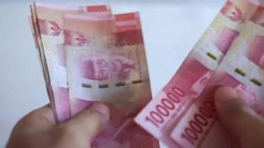 Adamın eli 100.000 rupia sayıyor. Beyaz bir arka planda Endonezya parası.