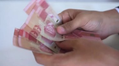 Adamın eli 100.000 rupia sayıyor. Beyaz bir arka planda Endonezya parası.