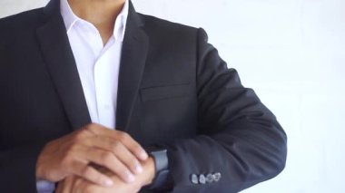 Takım elbiseli bir adam elindeki akıllı saati kontrol ediyor.