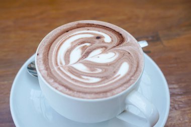 Bir fincan kahve ve ahşap bir masanın üstünde latte sanatı.