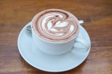 Bir fincan kahve ve ahşap bir masanın üstünde latte sanatı.