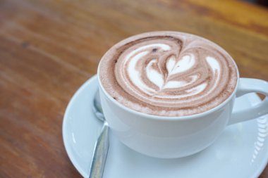 Bir fincan kahve ve ahşap bir masanın üstünde latte sanatı.