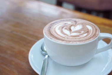 Bir fincan kahve ve ahşap bir masanın üstünde latte sanatı.