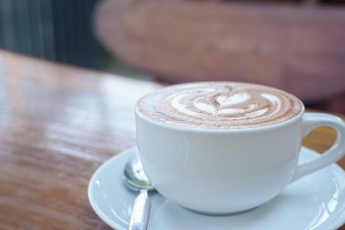 Bir fincan kahve ve ahşap bir masanın üstünde latte sanatı.