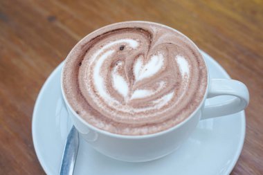 Bir fincan kahve ve ahşap bir masanın üstünde latte sanatı.