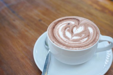 Bir fincan kahve ve ahşap bir masanın üstünde latte sanatı.