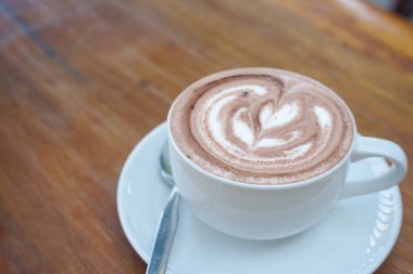 Bir fincan kahve ve ahşap bir masanın üstünde latte sanatı.