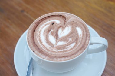 Bir fincan kahve ve ahşap bir masanın üstünde latte sanatı.