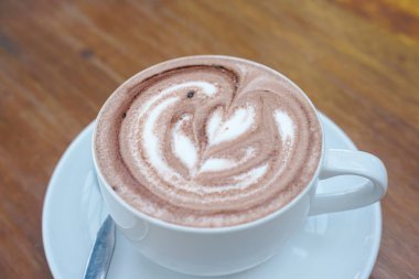 Bir fincan kahve ve ahşap bir masanın üstünde latte sanatı.