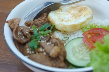 Üzerine ızgara sığır eti, kızarmış yumurta ve rengarenk sebzeler konmuş canlı bir kase pirinç.