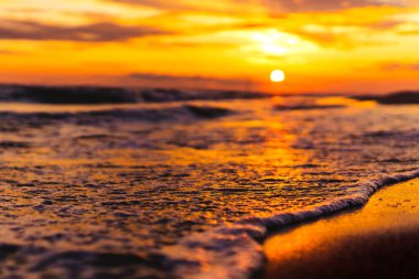 Beautiful sunset on the beach in Montenegro in summer. Natural, warm lightning. Waves are flooding the shore. Red, intense sunset in the background. The sea and the beach on golden hour. Summer beach time and warm weather. Memories. 