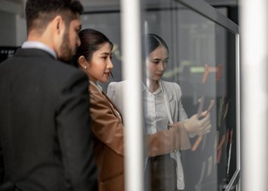 İş adamları tartışır, fikir alışverişinde bulunur ve yapışkan notlar kullanarak yeni perspektifler geliştirir. Bir takım olarak çalışmak, şirket için yenilikçi fikirler ve potansiyel çözümler üretmeye yardımcı olur..