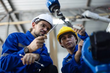 Robot teknisyenleri güvenlik onarımı için tornavida ve kerpetenle bileşenleri sıkılaştırıp gevşetiyorlar. Akım, voltaj, direnç, kapasite, dijital klemp ölçer ile sıcaklık ölçülüyor.