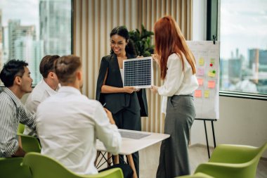 In multicultural workspace, innovative project manager present sustainable solar panel product, fostering collaboration and diversity among colleagues, aiming for efficient, renewable energy solution