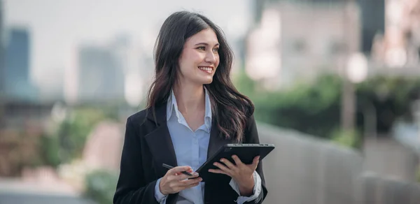 A determined and confident executive woman proudly leads organization, exemplifying exceptional leadership, commitment, strategic thinking while overseeing daily operations with her tablet in hand.
