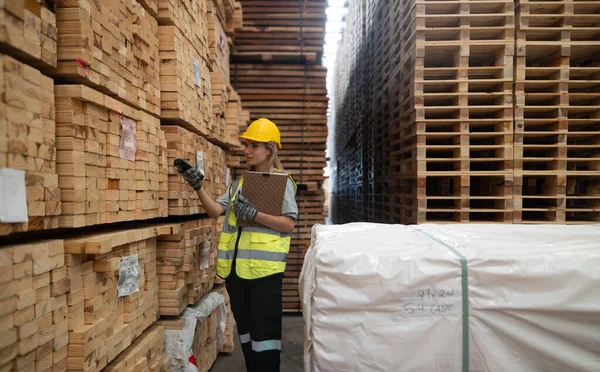 木材パレット倉庫のロジスティクスワーカーは ソフトウェア バーコードスキャナ ノートを含む商品の流れを管理する技術的なツールを使用して 正確にラベルを付ける 工場の倉庫で製品を検証します — ストック写真