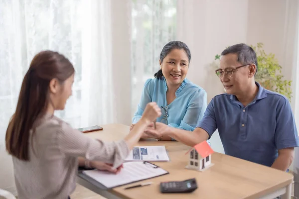 Elderly couples satisfying service in purchasing retirement residence. A detailed contract with saleswoman ensures a smooth transition, including key handovers after agreement on terms and conditions