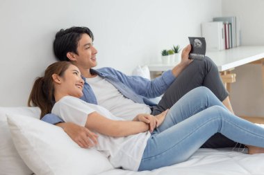 Asyalı çiftler ultrason görüntülerini tararken hamileliğin coşkusunu ve heyecanını kucaklarlar. Bebeğin rahmindeki sağlık, cinsiyet ve gelişimi ortaya çıkar. Mutluluk ve memnuniyet aile içinde bağı güçlendirir.