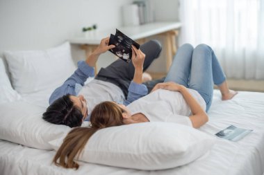 Asyalı çiftler ultrason görüntülerini tararken hamileliğin coşkusunu ve heyecanını kucaklarlar. Bebeğin rahmindeki sağlık, cinsiyet ve gelişimi ortaya çıkar. Mutluluk ve memnuniyet aile içinde bağı güçlendirir.