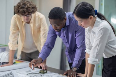 Mimarlardan oluşan çok kültürlü bir ekip, düşük karbonlu bir inşaat projesinde işbirliği yapıyor, planları analiz ediyor, taslakları hazırlıyor, çevre dostu inşaat için hassas yapılar ve malzemeler hesaplıyor.