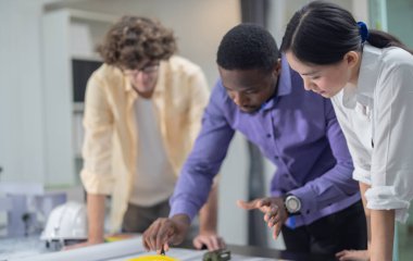 Mimarlardan oluşan çok kültürlü bir ekip, düşük karbonlu bir inşaat projesinde işbirliği yapıyor, planları analiz ediyor, taslakları hazırlıyor, çevre dostu inşaat için hassas yapılar ve malzemeler hesaplıyor.