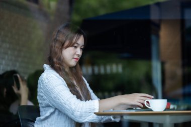 Düşünceli bir Asyalı kadın, rahat bir kafede laptopuyla çalışırken kırmızı kulaklıkla müzik dinliyor..