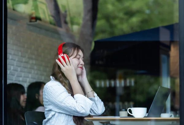 Kontemplativ Asiatisk Kvinna Lyssnar Musik Röda Hörlurar Medan Hon Arbetar — Stockfoto