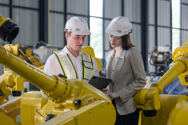 Senior engineer provides guidance to a trainee amidst robotic arms in a high-tech warehouse factory setting.