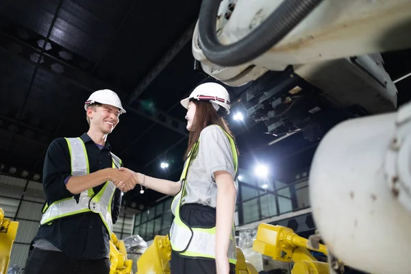 Senior engineer provides guidance to a trainee amidst robotic arms in a high-tech warehouse factory setting.