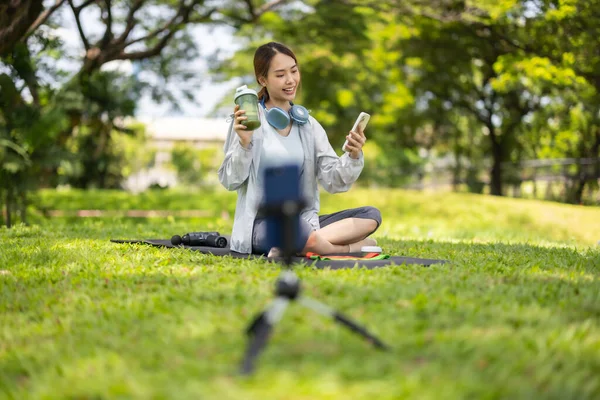 Bir kadın sosyal medya etkeni sohbetin ortasında, yemyeşil bir çimenlikte otururken çevrimiçi izleyicilerine protein tozu içeceği sergilerken yakalanıyor..