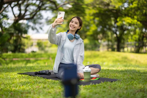 Bir kadın sosyal medya etkeni sohbetin ortasında, yemyeşil bir çimenlikte otururken çevrimiçi izleyicilerine protein tozu içeceği sergilerken yakalanıyor..
