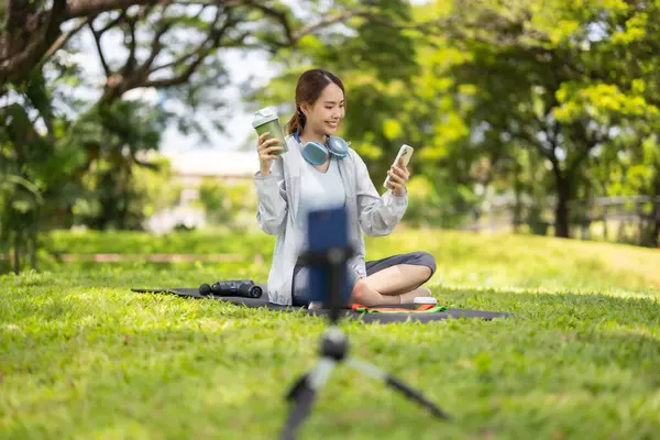 Bir kadın sosyal medya etkeni sohbetin ortasında, yemyeşil bir çimenlikte otururken çevrimiçi izleyicilerine protein tozu içeceği sergilerken yakalanıyor..