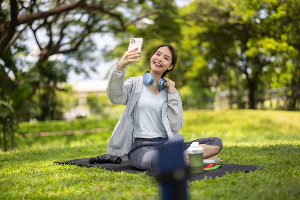 Bir kadın sosyal medya etkeni sohbetin ortasında, yemyeşil bir çimenlikte otururken çevrimiçi izleyicilerine protein tozu içeceği sergilerken yakalanıyor..