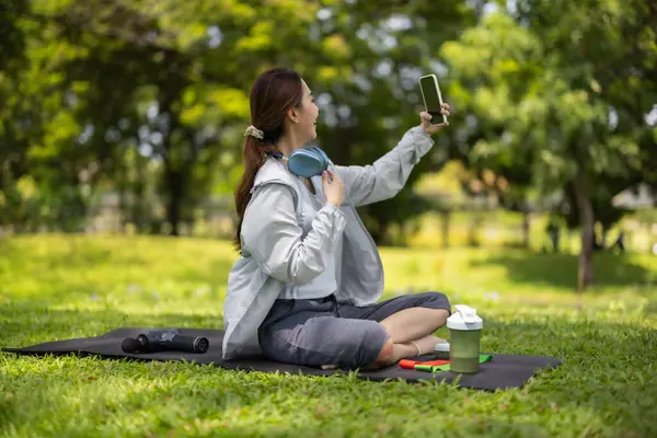 Bir kadın sosyal medya etkeni sohbetin ortasında, yemyeşil bir çimenlikte otururken çevrimiçi izleyicilerine protein tozu içeceği sergilerken yakalanıyor..