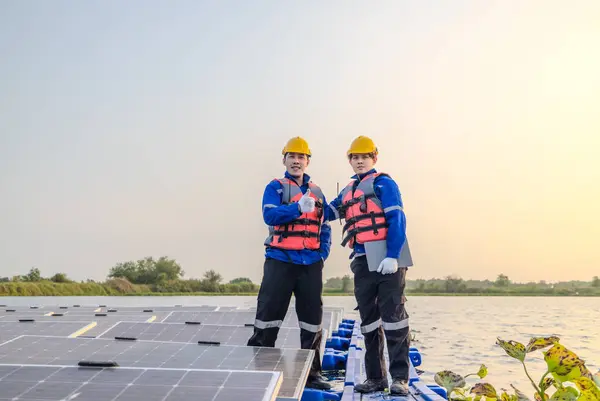 2人の技術者は 夜の光が背景で衰退するように 浮遊太陽光ファームの広大な配列のソーラーパネルの中でポイズされ 注意深く立っています — ストック写真