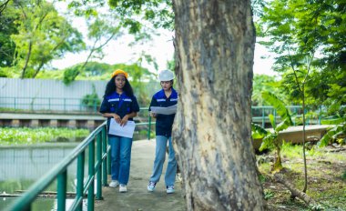 İki Çevre Mühendisi planları analiz edip tartışıyor. Yeni projelerinin karbon ayak izini azaltmak için yenilikçi stratejiler ve sürdürülebilir uygulamalar saptamak.