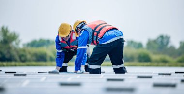 Koruyucu teçhizat ve kask takan iki güneş mühendisi standart gereksinimleri karşılamak için geniş bir dizi yüzen güneş panelinin hizalamalarını, istikrarını ve kalite güvencesini görsel olarak inceler.