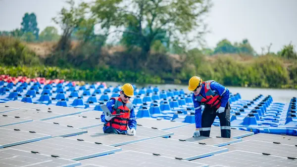 两名戴防护装置和钢盔的太阳能工程师目视检查了一大批浮动太阳能电池板的配合 稳定性和质量保证 以满足标准要求 — 图库照片