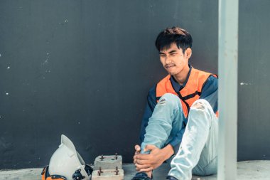 Asyalı HVAC mühendisi iş sırasında ciddi bacak yaralanması yaşadı. Acil ilk yardım ve iş arkadaşlarının yardımı gereklidir. Yüzündeki acı ifadeleri fiziksel ve duygusal tepkileri ifade eder..