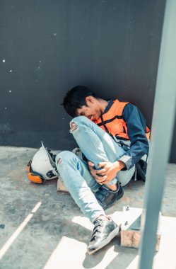 Asyalı HVAC mühendisi iş sırasında ciddi bacak yaralanması yaşadı. Acil ilk yardım ve iş arkadaşlarının yardımı gereklidir. Yüzündeki acı ifadeleri fiziksel ve duygusal tepkileri ifade eder..