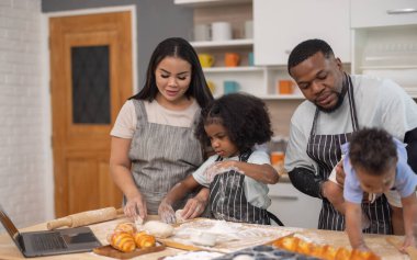 Un ve ekmek ruloları ile çevrili bir dizüstü bilgisayarı rehberlik etmek için birlikte yemek pişirmekten mutlu olan bir aile..