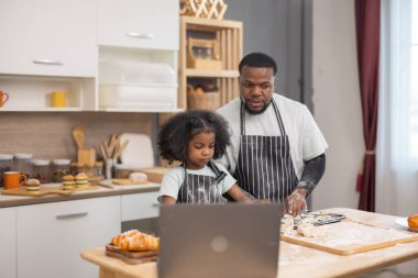 Un ve ekmek ruloları ile çevrili bir dizüstü bilgisayarı rehberlik etmek için birlikte yemek pişirmekten mutlu olan bir aile..